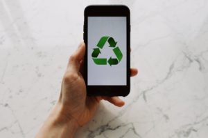 A smartphone with a recycling image on the screen, held by a hand.